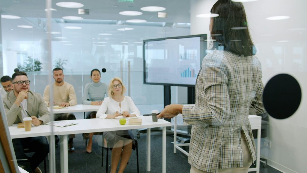 Une femme fait une présentation devant un public attentif dans un bureau moderne.